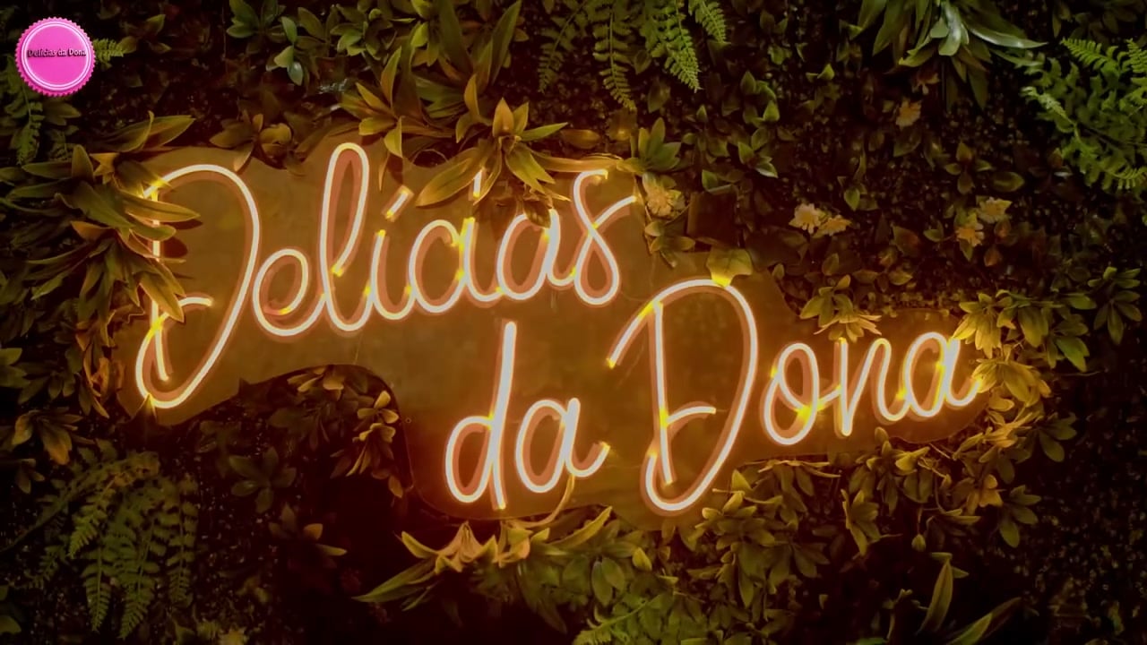 Letreiro em néon «Delícias da Dona» sobre uma parede de folhagem
